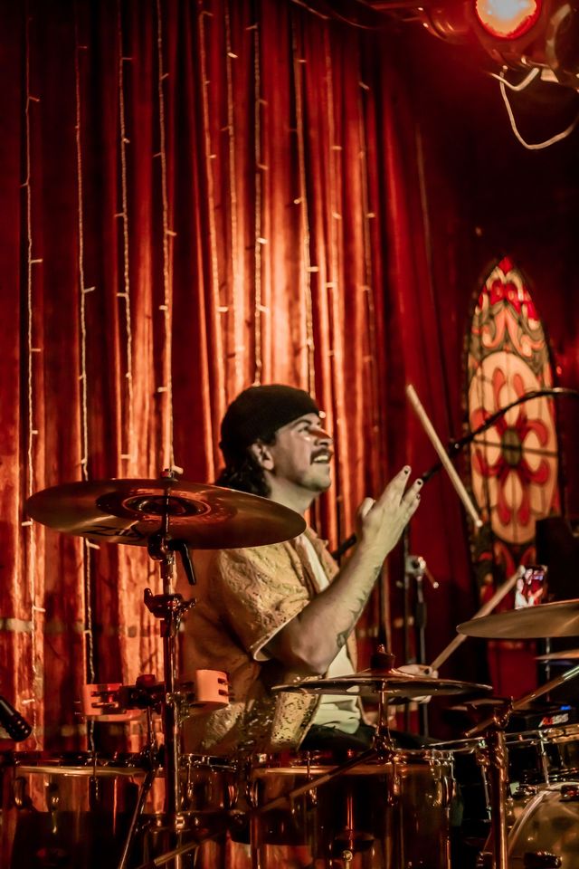 Mikey playing drums in front of a red curtain
