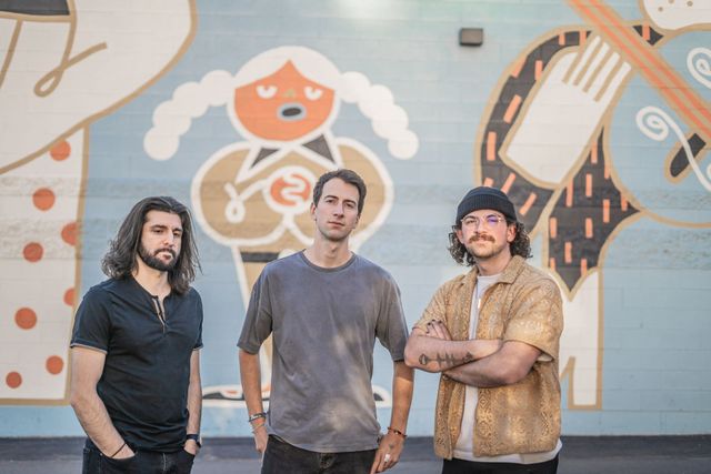 Three band members in front of a wall mural